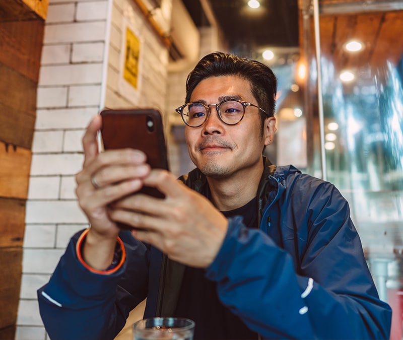 Man using smartphone in a cafe, focused on browsing or communicating with others.