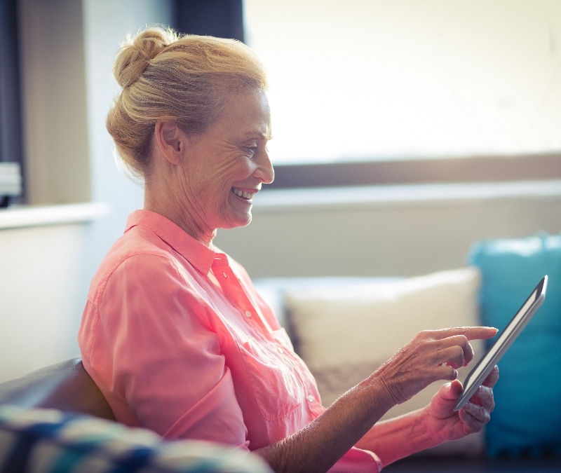 An older woman smiles as she looks at her phone.