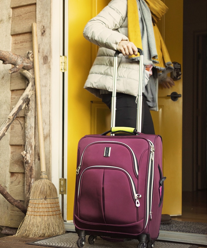 A woman with a rolling luggage bag enters the front door of a home, worried it’s an Airbnb scam.