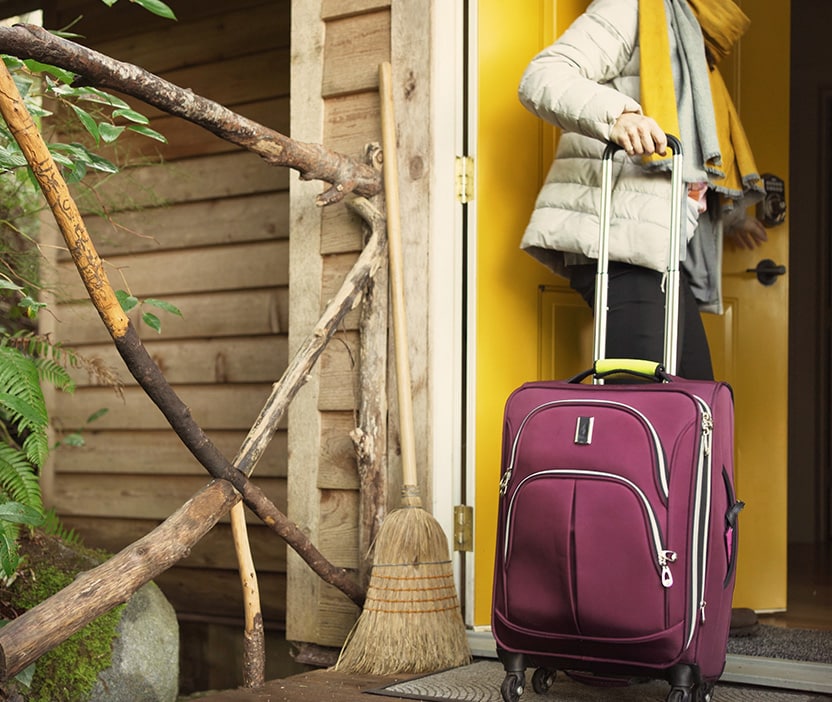 A woman with a rolling luggage bag enters the front door of a home, worried it’s an Airbnb scam.