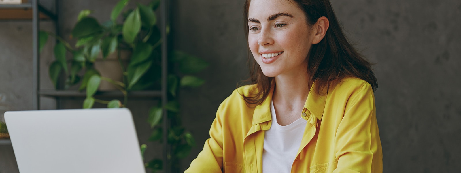 A woman with a yellow shirt looking at her laptop learning about the benefits of a VPN.