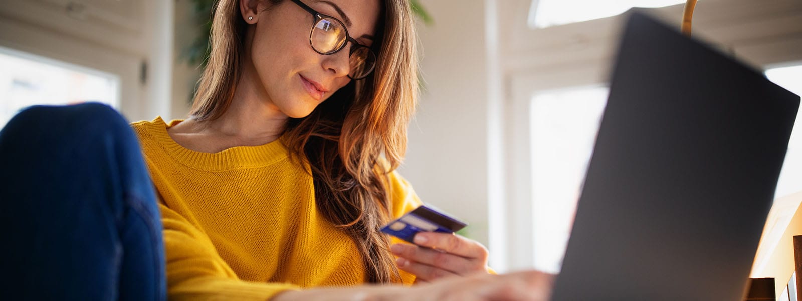 A woman looks at her credit card while using a computer to look up information on Black Friday scams.