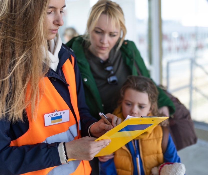 A disaster aid worker holds a clipboad while a mom and child look on.