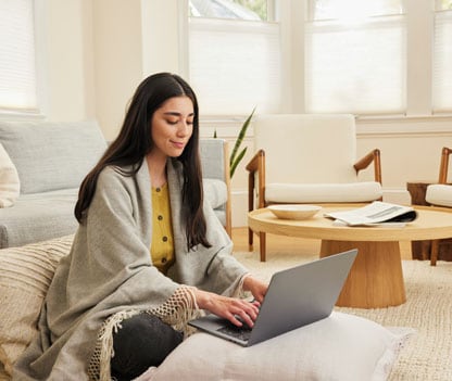 A woman playing video games on her laptop while relaxing on a pillow.