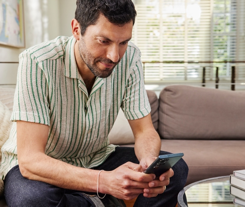 A man sitting on a couch looks down at his phone and learns about lateral movement attacks.