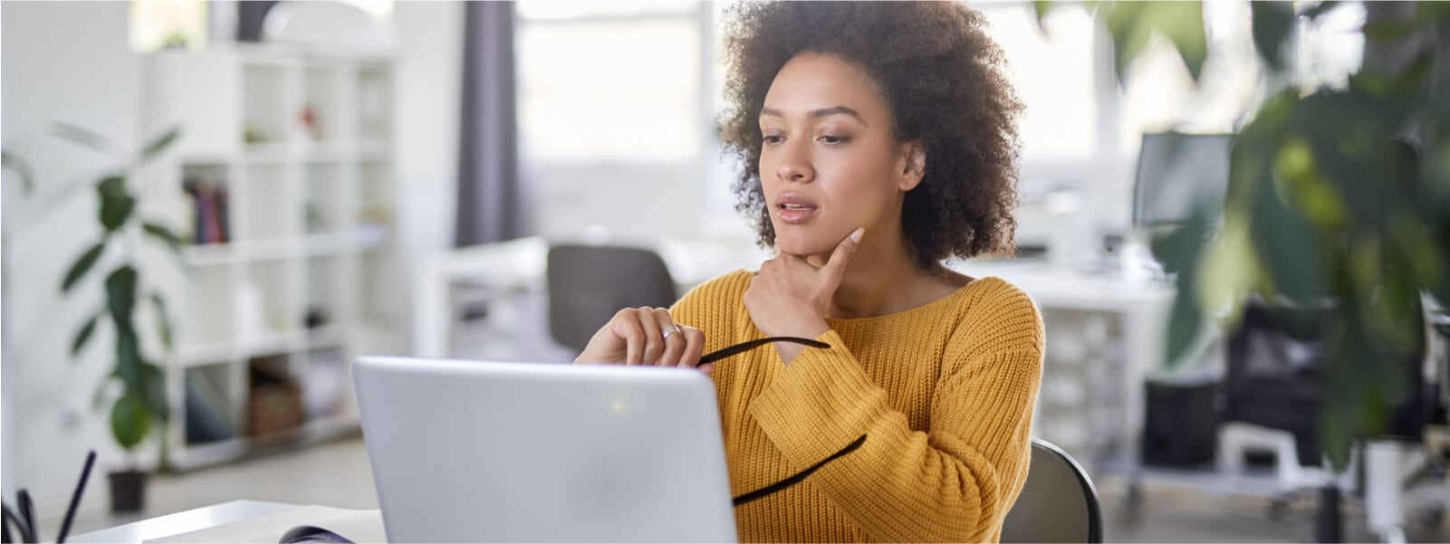 A woman wears a  yellow sweater looking at her computer and determining whether or not she is a victim of a LinkedIn scam.