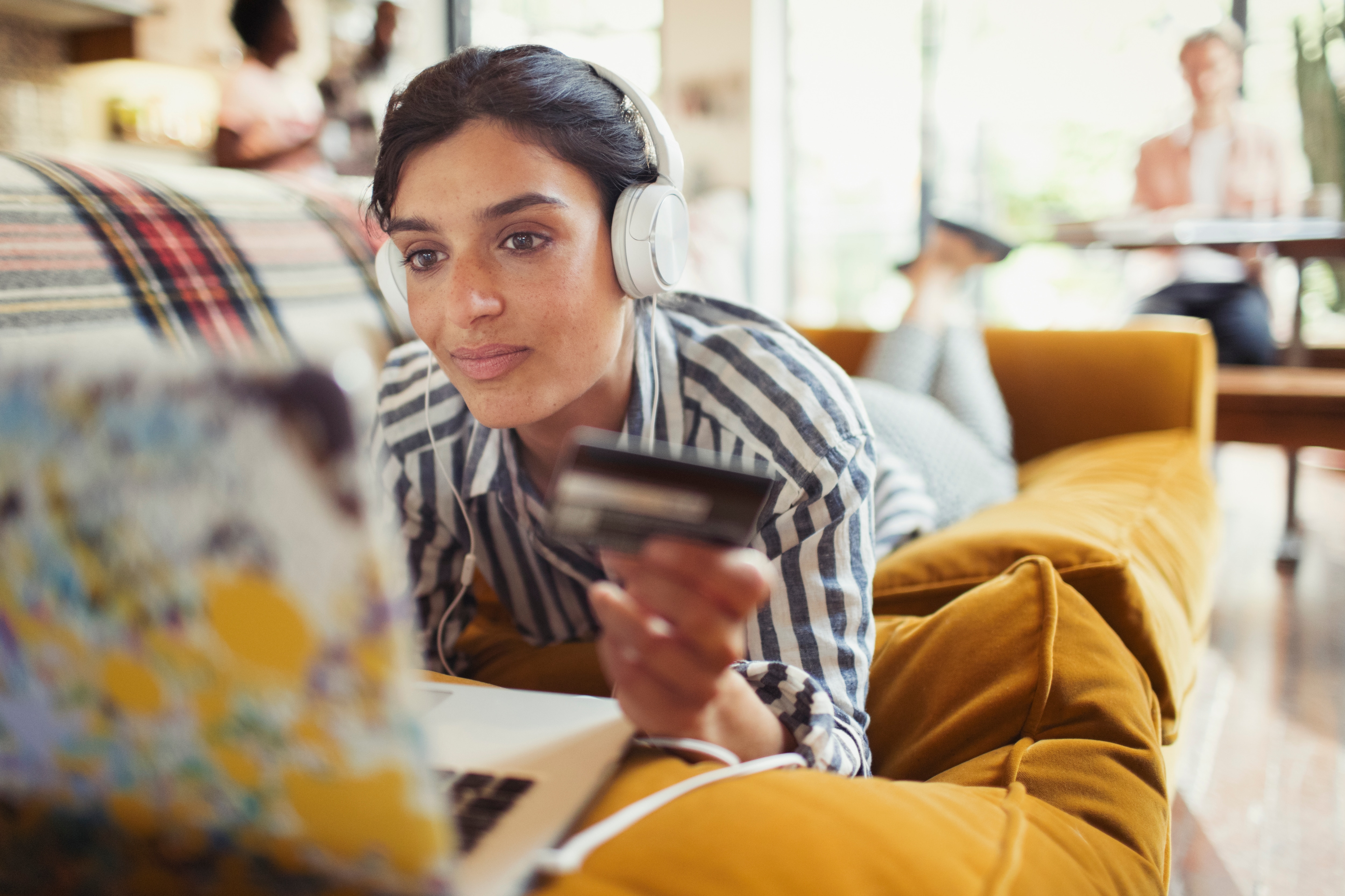 Woman lying down looks at her computer while holding a credit card.