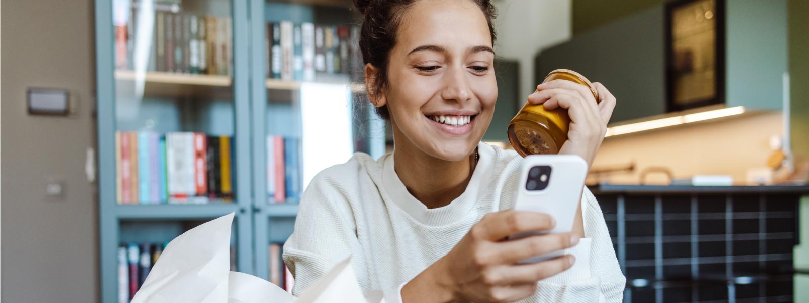 Photo of a woman looking at OfferUp on her phone while sitting in a kitchen.