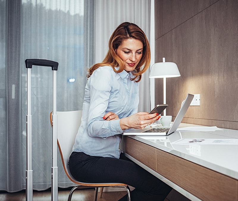 A woman using her laptop and cell phone while sitting at a desk.