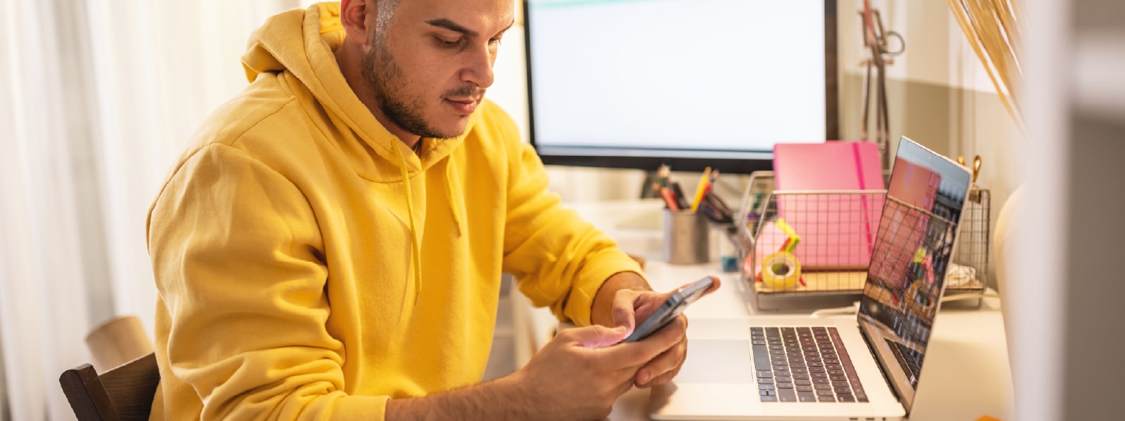 A man in a yellow sweatshirt looking at his phone learning about social media scams.