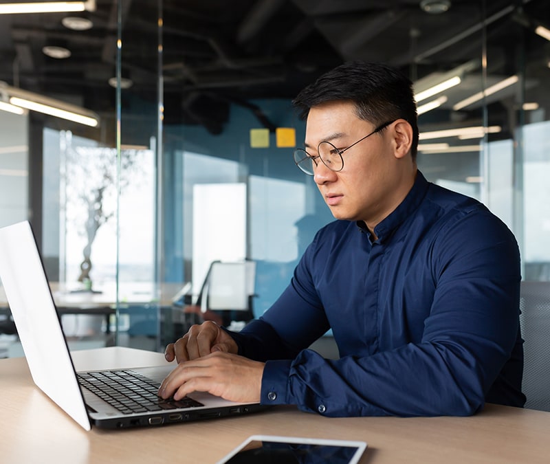 A man wearing glasses concentrates on his laptop, engrossed in his tasks.