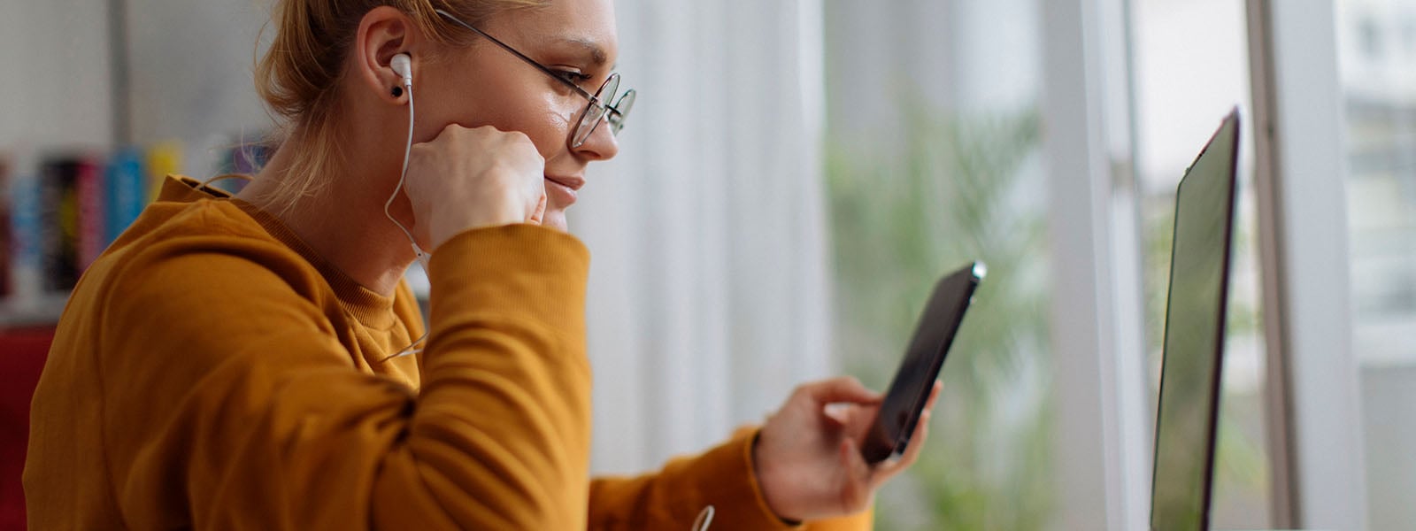 Woman sitting in front of a computer entering 2FA on her phone.