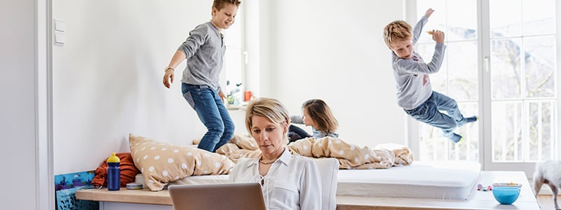 Mother connecting to remote access computer while children play in background.