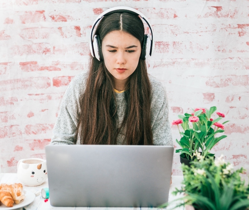 A young woman sits looking at her laptop, learning about online scams.