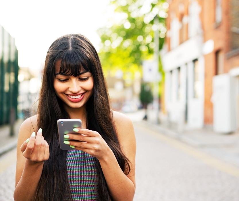 A young woman looks down at her phone and smiles at instructions on how to use her zodiac sign to create stronger passwords.