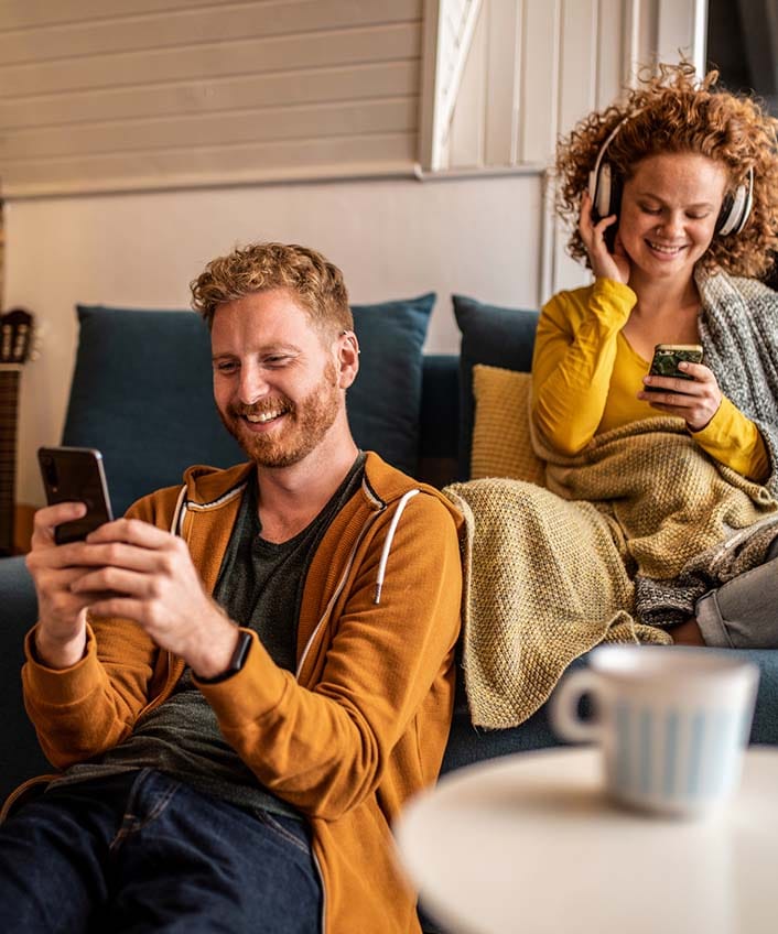 Two friends sit on a couch and use the guest Wi-Fi network to look at their phones.