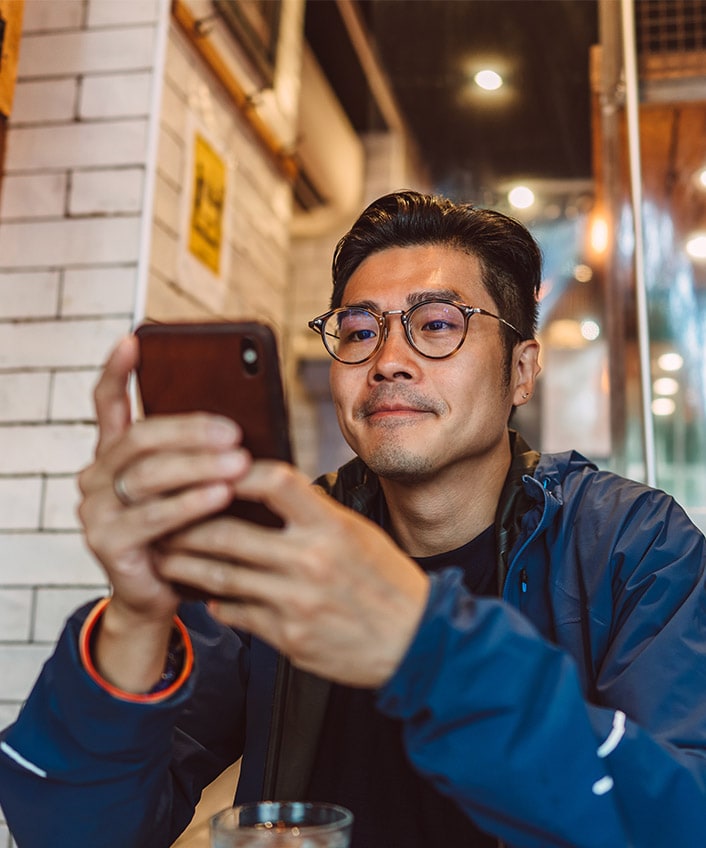 Man using smartphone in a cafe, focused on browsing or communicating with others.