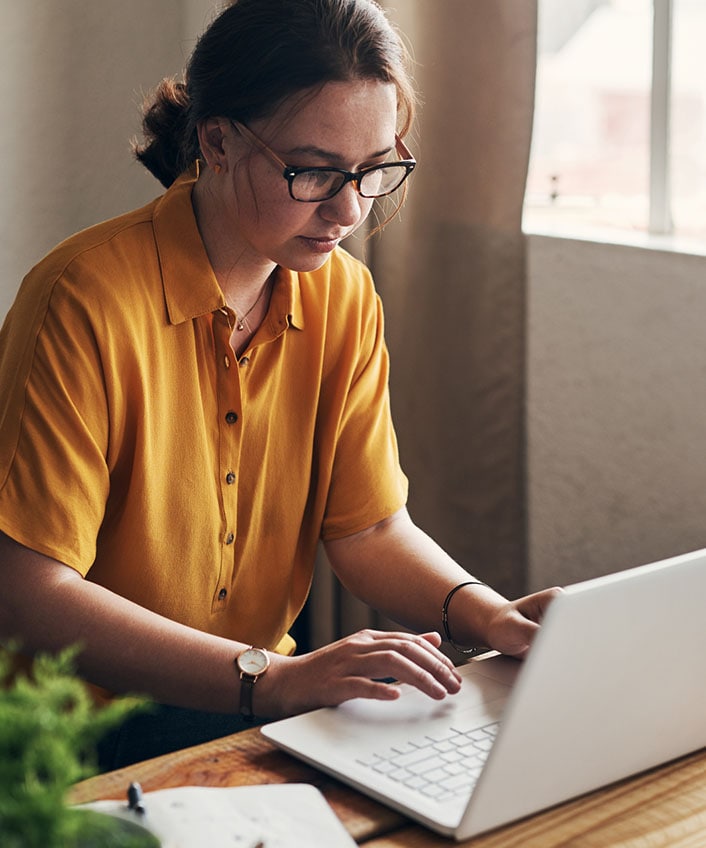 A person in a yellow shirt using a laptop computer to learn how to check if a website is safe.