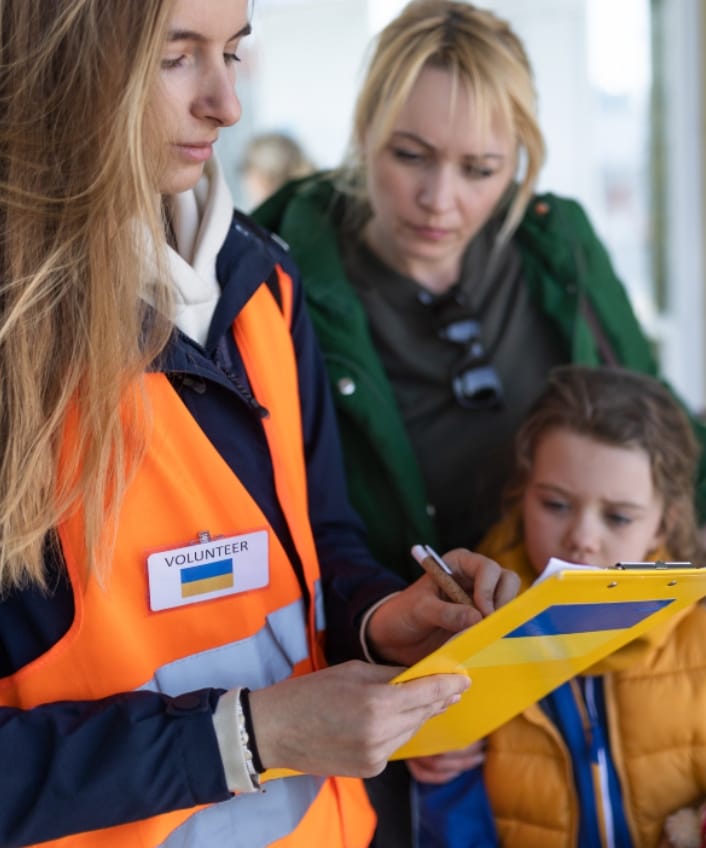 A disaster aid worker holds a clipboad while a mom and child look on.