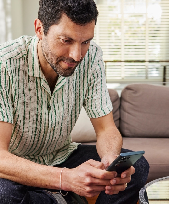 A man sitting on a couch looks down at his phone and learns about lateral movement attacks.