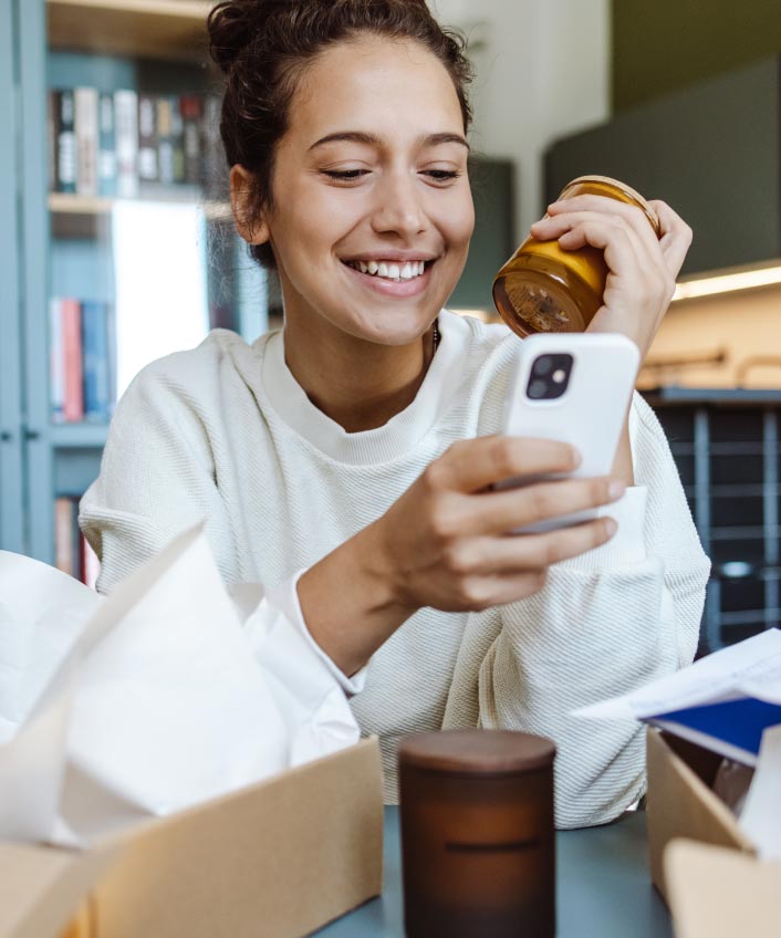 Photo of a woman looking at OfferUp on her phone while sitting in a kitchen.