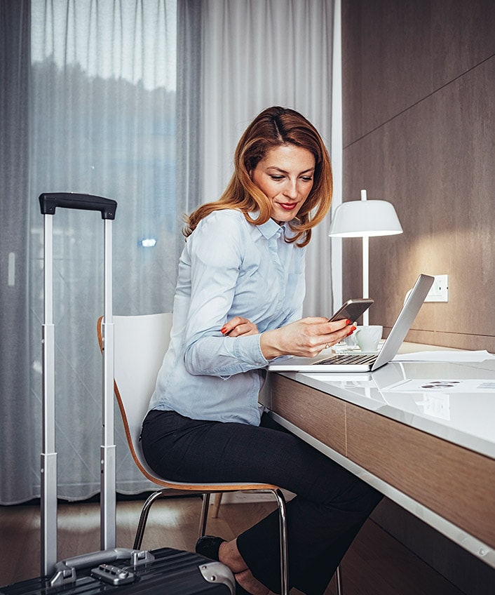 A woman using her laptop and cell phone while sitting at a desk.