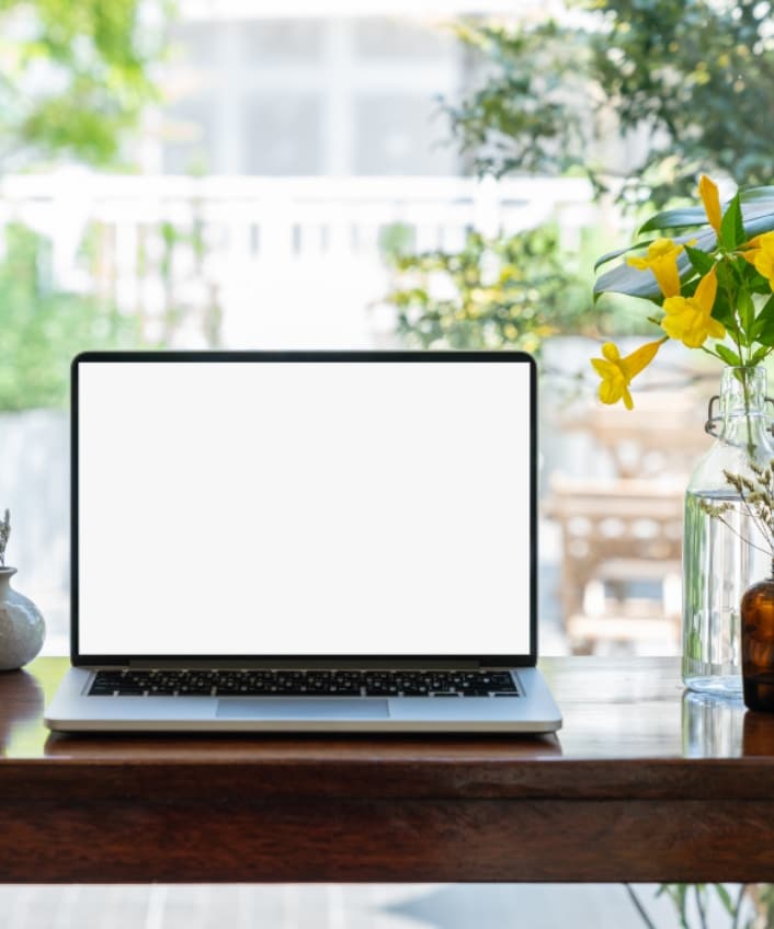 A laptop with a blank screen representing the Phantom Hacker sits on a high table in a coffee shop window with plants around it.