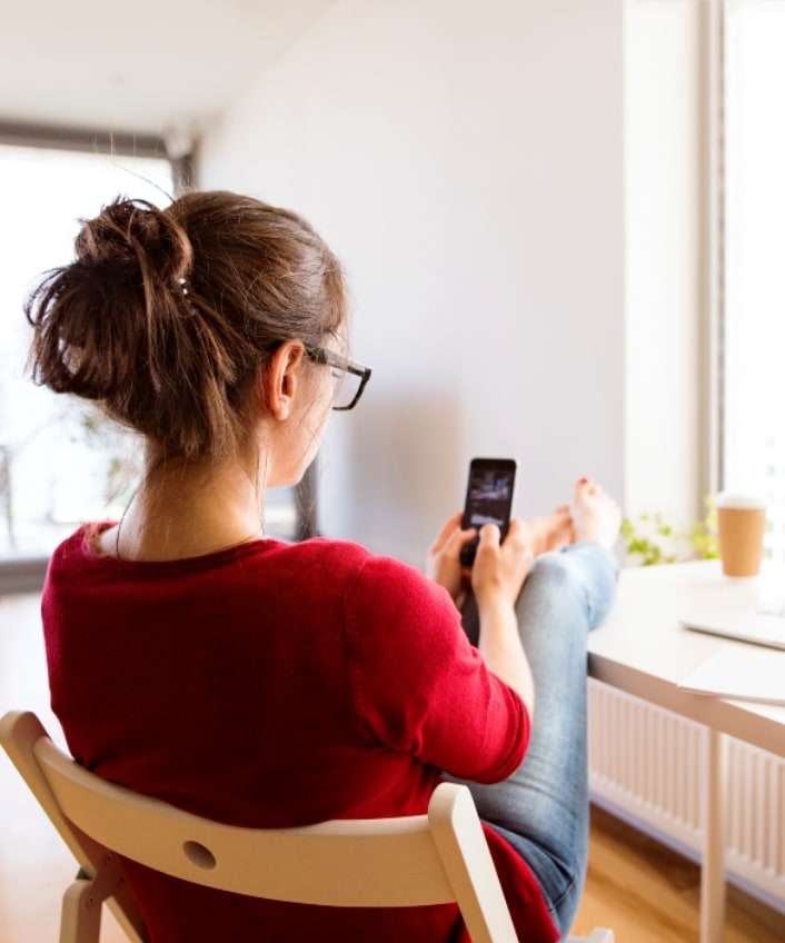 A woman sits with her feet up on a table with a laptop and a phone in front of her.