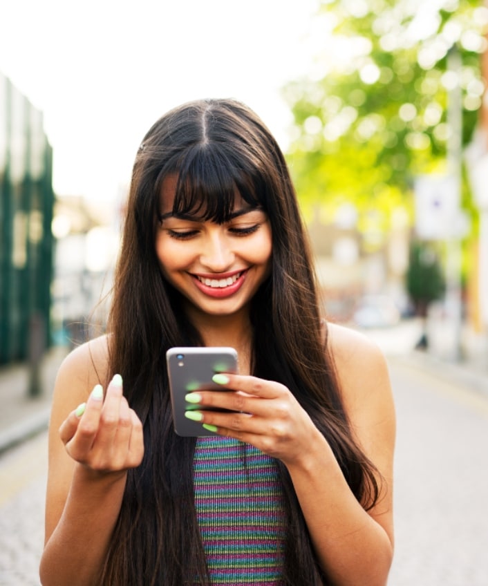 A young woman looks down at her phone and smiles at instructions on how to use her zodiac sign to create stronger passwords.