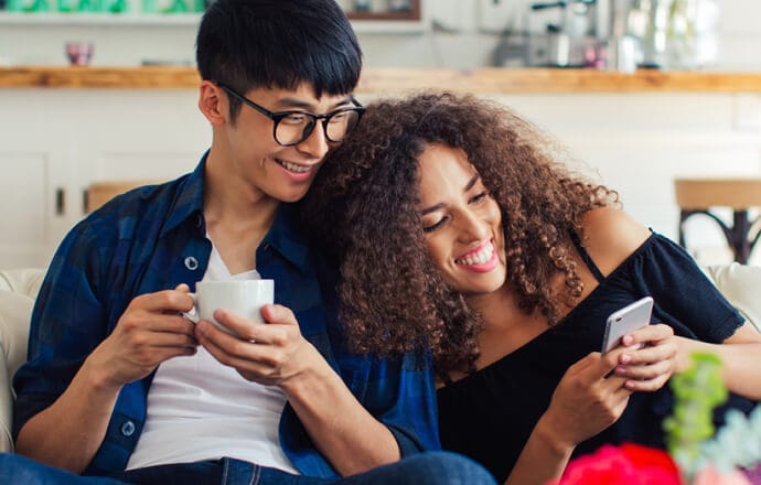 man and women on sofa looking at cell phone protected by Norton 360 for mobile.