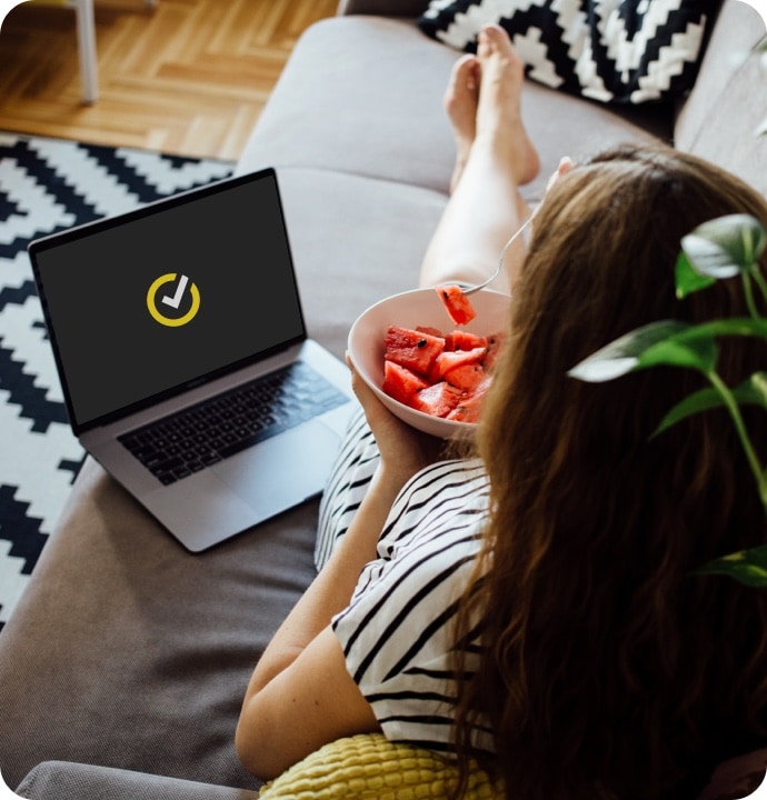 girl eating watermelon on sofa using laptop launching Norton 360 AntiVirus Plus.