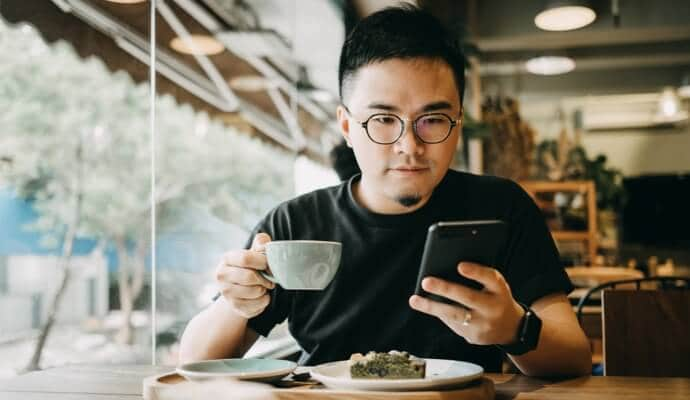 Man enjoying coffee  looking at cell phone launching Norton 360 Standard.